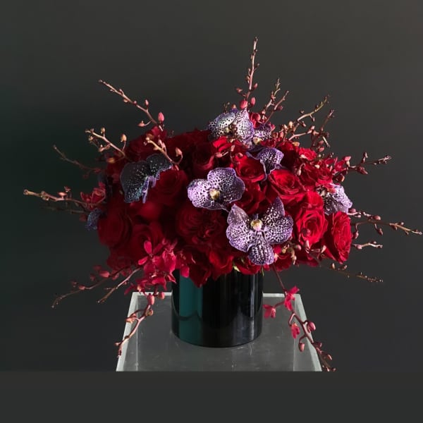 Red rose arrangement with spotted orchids in a black vase
