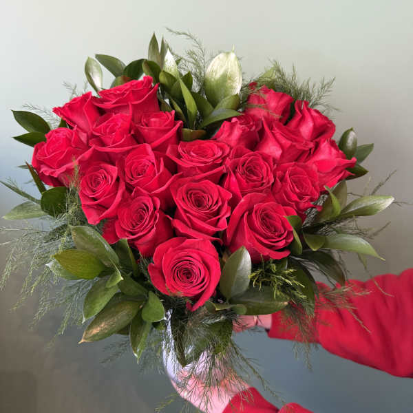 Handheld bouquet of red roses with green foliage
