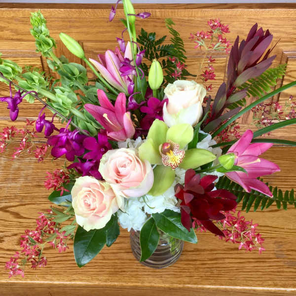Mixed bouquet of roses, orchids, and lilies in a glass vase