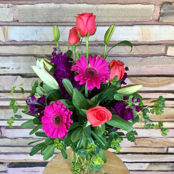 Pink roses and gerbera daisies in a glass vase with purple flowers
