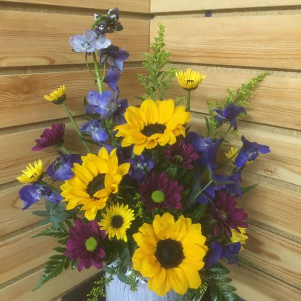 Bouquet of yellow sunflowers and purple daisies in a white vase