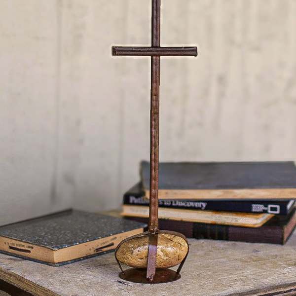 Rustic metal cross standing on a wooden base with a stone accent