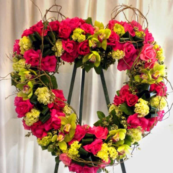 Heart-shaped floral wreath of pink roses and yellow blooms on an easel