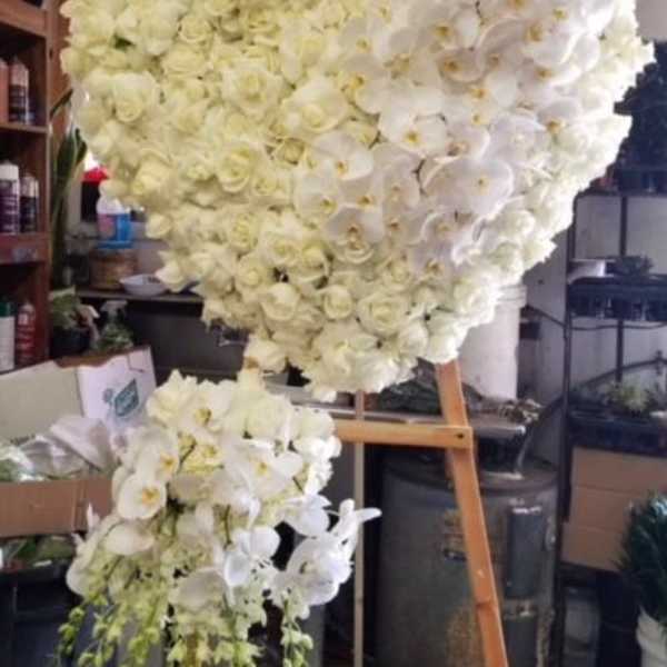 Heart-shaped floral arrangement of white roses and orchids on an easel