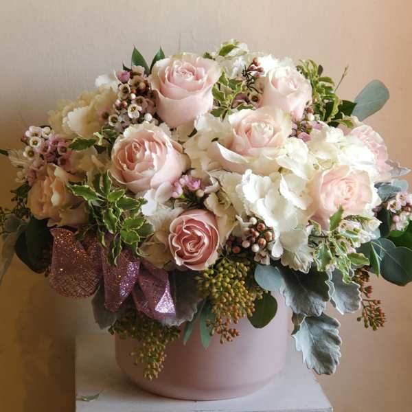 Blush roses and white flowers in a pink vase with a ribbon