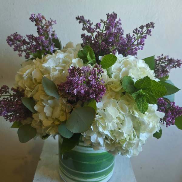 White hydrangeas and purple lilacs in a green-striped vase