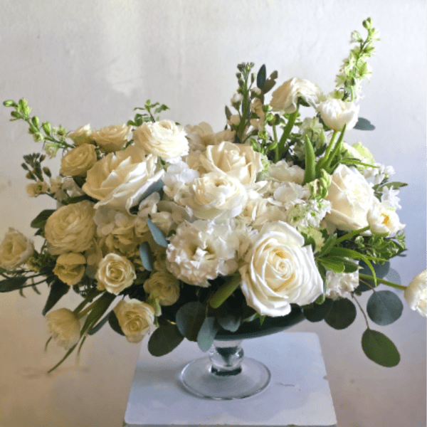 Low arrangement of white roses and other white blooms in a glass pedestal bowl