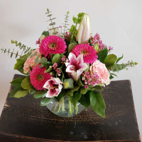 Bright pink and blush flower arrangement with lilies, gerbera daisies, and roses in a glass bowl vase