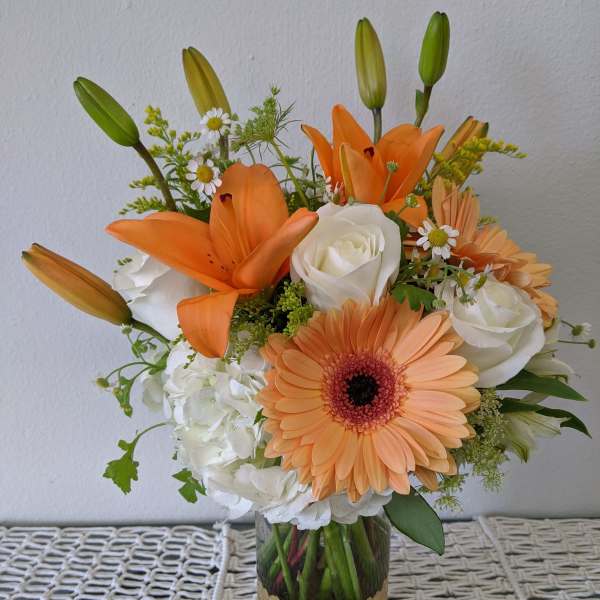 Orange lilies and peach gerbera daisies in a glass vase with white roses
