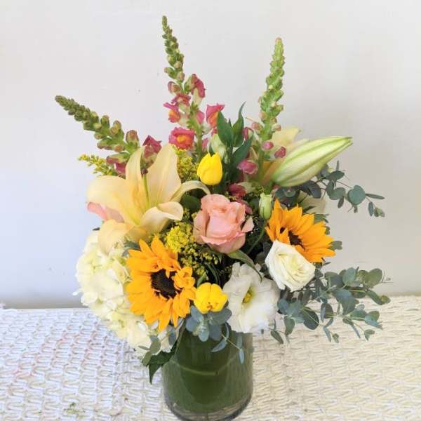 Mixed bouquet in a glass vase with sunflowers, lilies, roses, and tulips