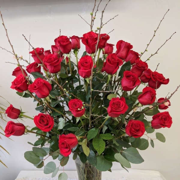 Red roses arranged in a clear glass vase with branching accents