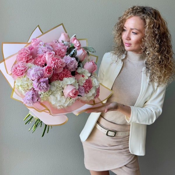 Large pink and white bouquet with roses and carnations held by a woman in a cream outfit