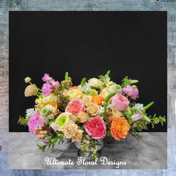 Mixed bouquet of pink, peach, orange, and cream flowers in a low vase