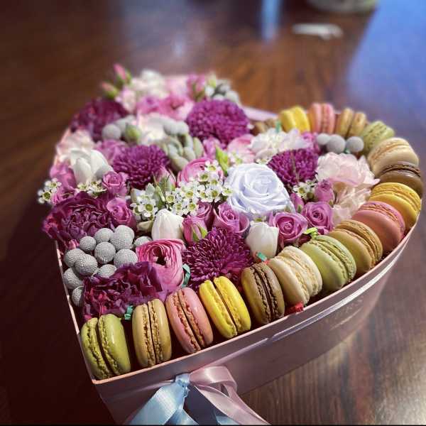 Heart-shaped box of pink and white flowers with colorful macarons around the edge