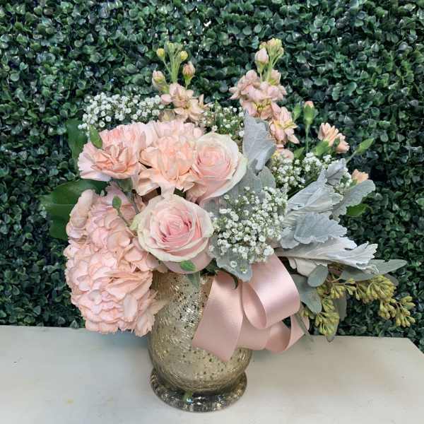 Pink roses and hydrangeas in a gold vase with a pink ribbon