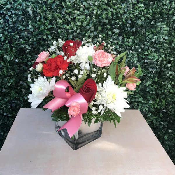Bouquet of red, pink, and white flowers in a glass vase with a pink ribbon