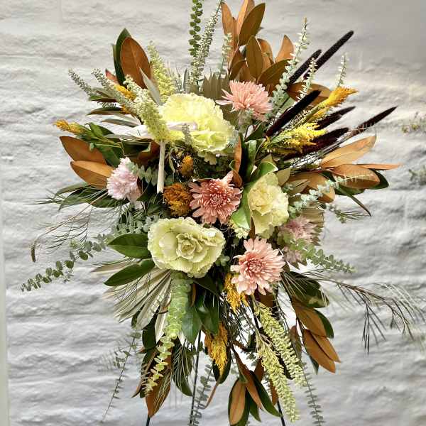 Tall floral spray with pale blooms and copper-toned foliage on a stand