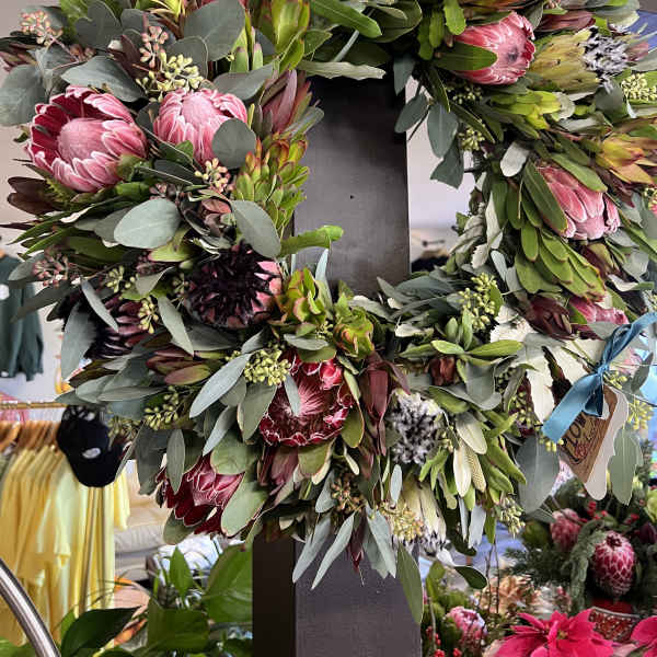 Large wreath of pink protea and eucalyptus on a dark stand