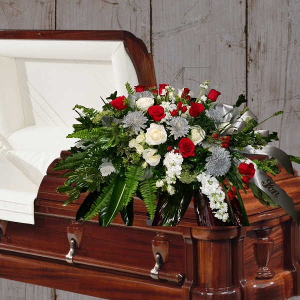 Casket spray of red and white roses with greenery on a wooden casket