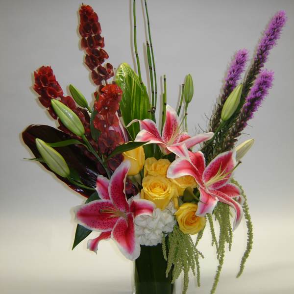 Mixed bouquet with pink lilies, yellow roses, and purple spikes in a glass vase