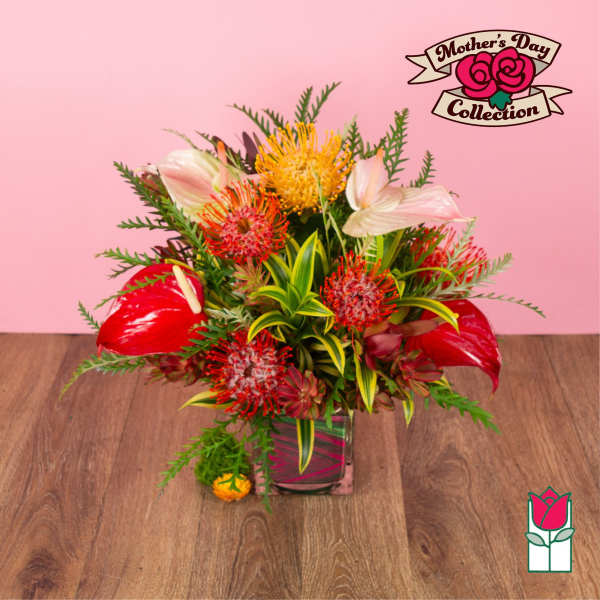 Bright tropical arrangement with red anthuriums and orange pincushion protea in a square glass vase