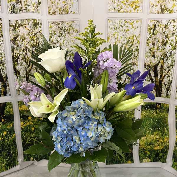 Bouquet of blue hydrangeas, white lilies, and purple flowers in a glass vase