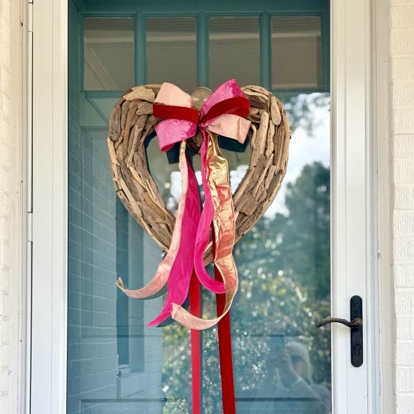 Heart-shaped twig wreath with pink and red ribbons on a glass door