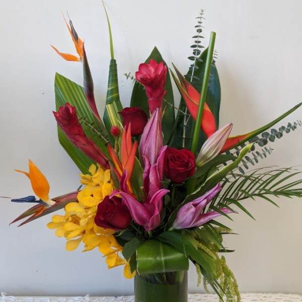 Tropical bouquet with red roses and orchids in a tall glass vase