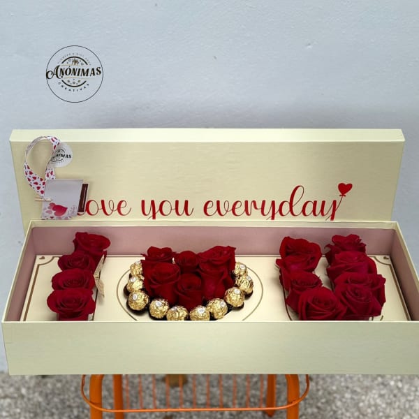 Cream gift box with red roses and gold-wrapped chocolates arranged around a heart of roses