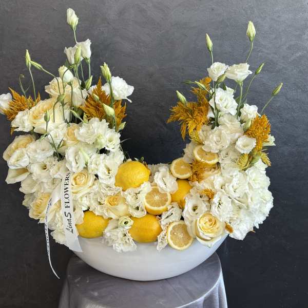 White and yellow floral arrangement in a white bowl with lemons and citrus slices