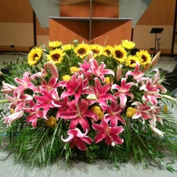 Large stage arrangement of pink lilies, yellow sunflowers, and yellow blooms in a low, wide design