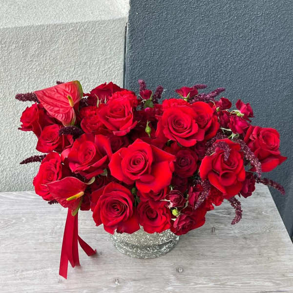 Red rose arrangement in a silver vase with burgundy accents
