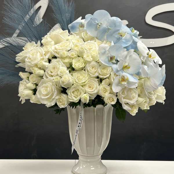 White roses and pale blue orchids in a white vase