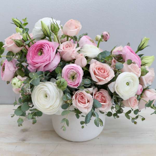 Low pastel arrangement of pink roses and ranunculus in a white ceramic bowl-style vase