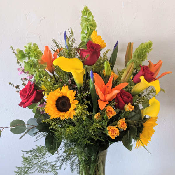 Mixed bouquet with sunflowers, roses, and calla lilies in a glass vase