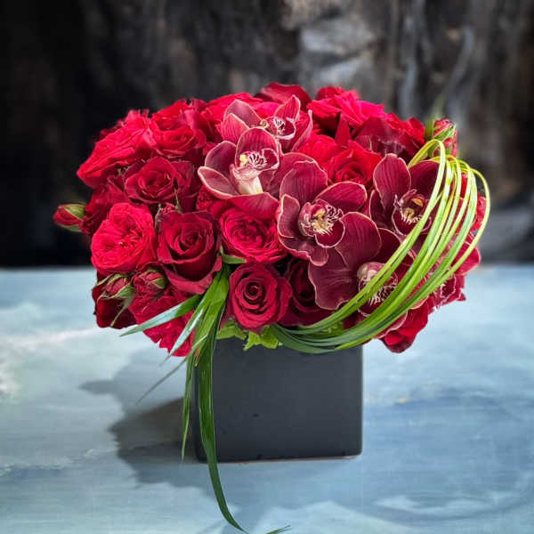 Red rose and orchid arrangement in a black square vase
