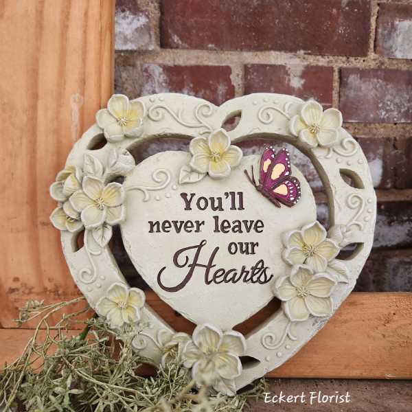 Heart-shaped decorative plaque with flowers and a butterfly, reading "You'll never leave our Hearts"