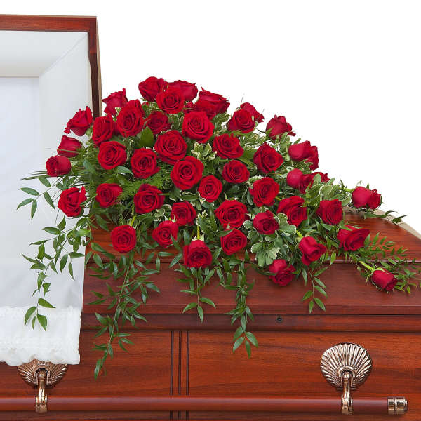 Red rose casket spray with cascading greenery on a wooden casket