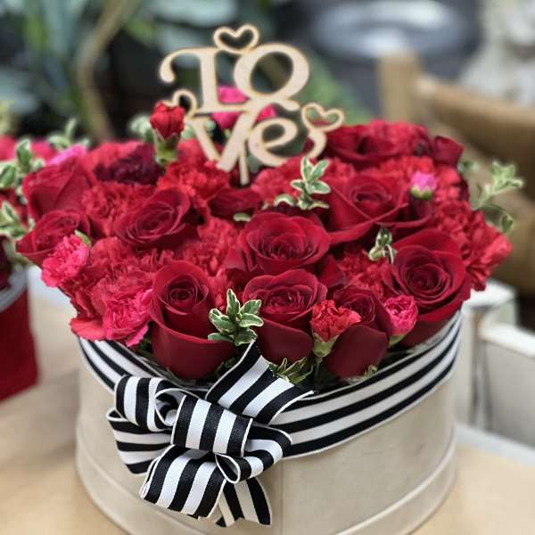 Heart-shaped box of red roses and carnations with a "Love" topper