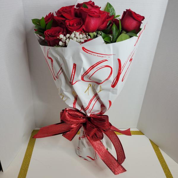 Bouquet of red roses with white filler flowers wrapped in white paper and a red ribbon