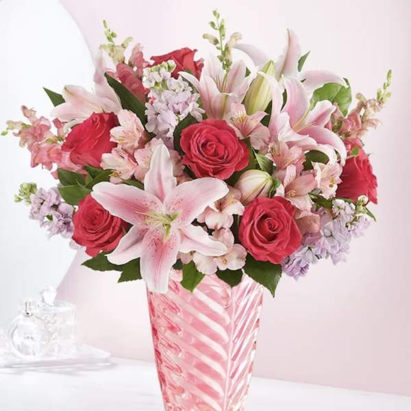 Pink lilies and red roses arranged in a striped glass vase