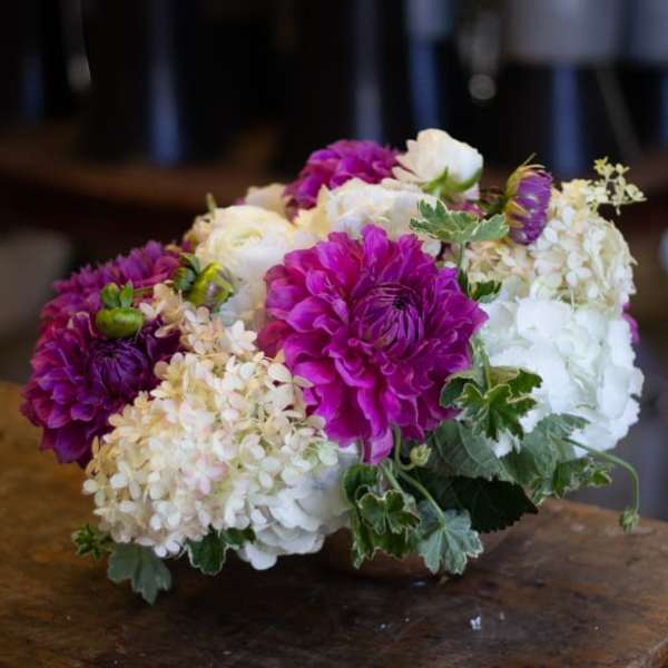 Low bouquet of purple, white, and cream flowers on a table