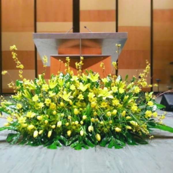 Large low arrangement of yellow lilies and tulips displayed on a stage in front of a podium