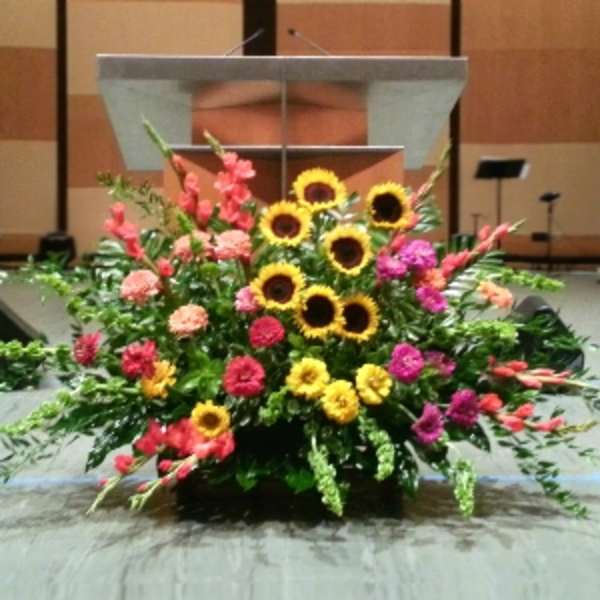 Large stage arrangement of yellow sunflowers with pink and orange flowers in front of a podium