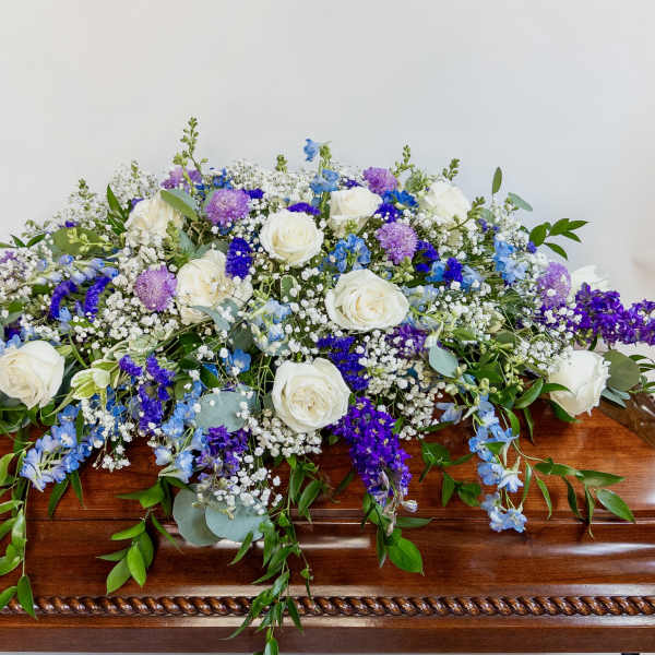 White roses and purple-blue flowers arranged on a wooden casket