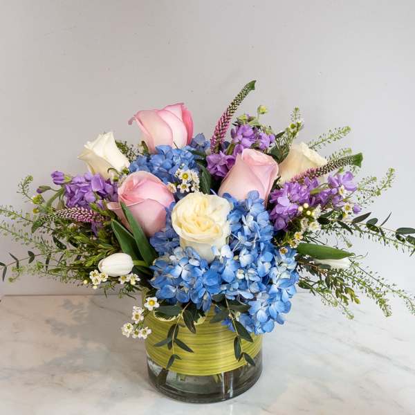 Pink and white roses with blue hydrangeas in a glass vase