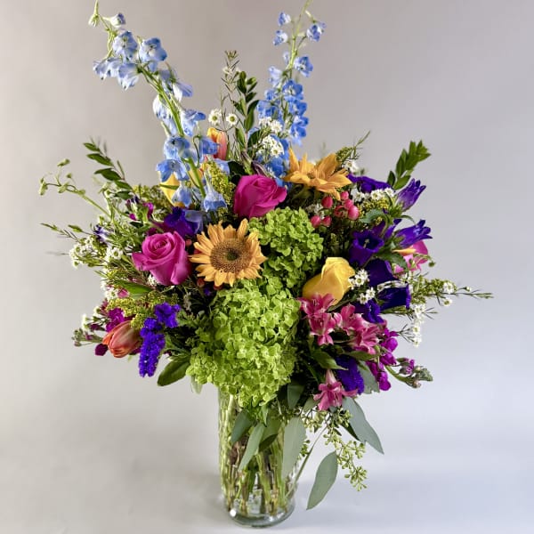 Mixed bouquet in a clear glass vase with blue, pink, yellow, and purple flowers