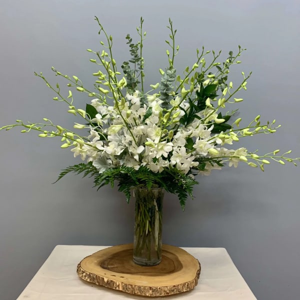 White orchid arrangement in a tall glass vase on a wood slice