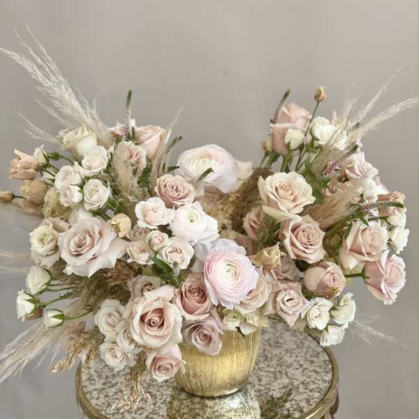 Blush and white rose arrangement in a gold vase with airy pampas grass