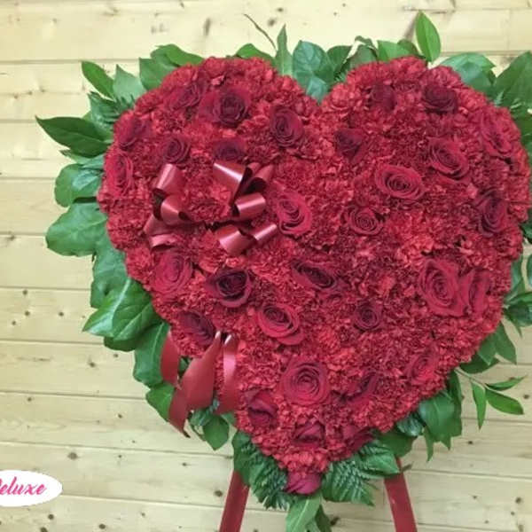 Heart-shaped red floral arrangement with ribbon accents and green leaves